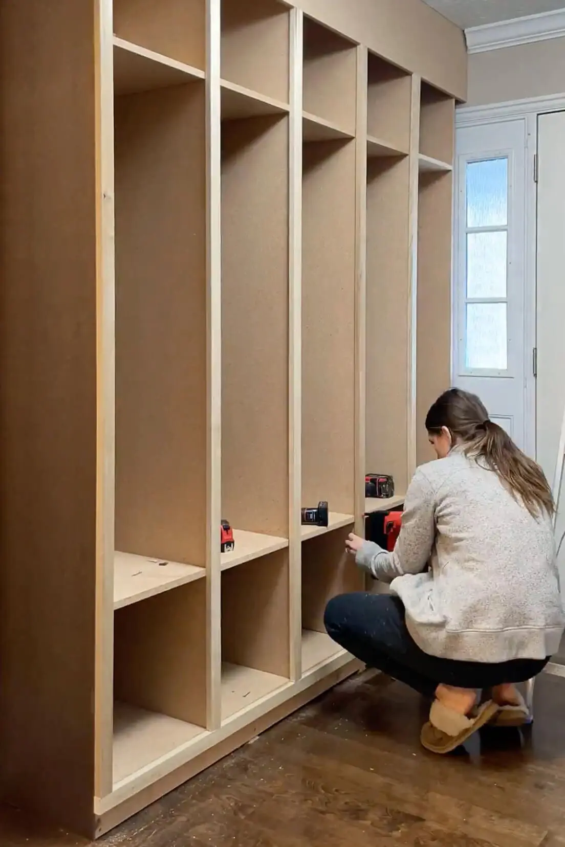 Using a nail gun to attach face frame pieces to individual storage cubbies, reinforcing the structure for a sturdy and seamless design.
